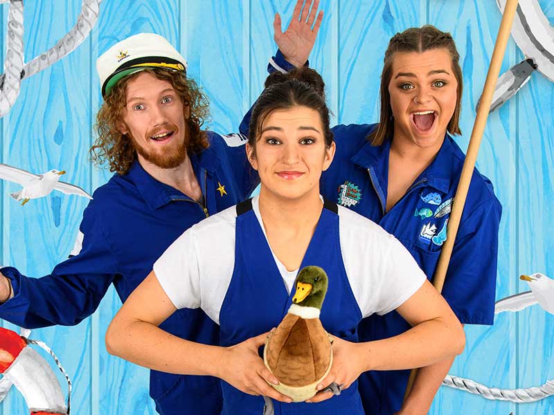 Three performers in overalls holding a duck.